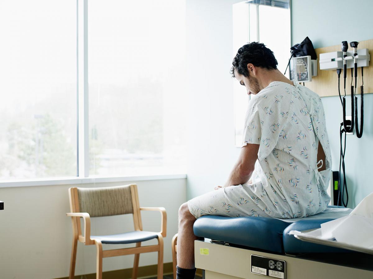 man sitting on the table in doctor's office wearing a hospital gown
